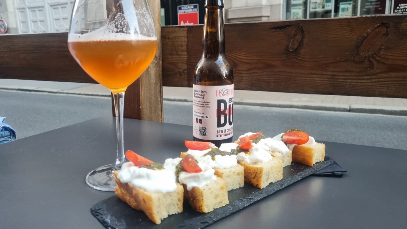 Tartines de focaccia à la burrata, pesto et tomate cerise, avec un verre de bière sans alcool Beach Bum en terrasse.